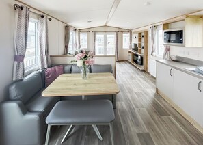 Een modern RV-interieur met een eethoek, zitplaatsen, een keuken met een magnetron en een televisie.
