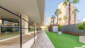 Um edifício moderno com fachada de vidro, deck de madeira e área ajardinada.