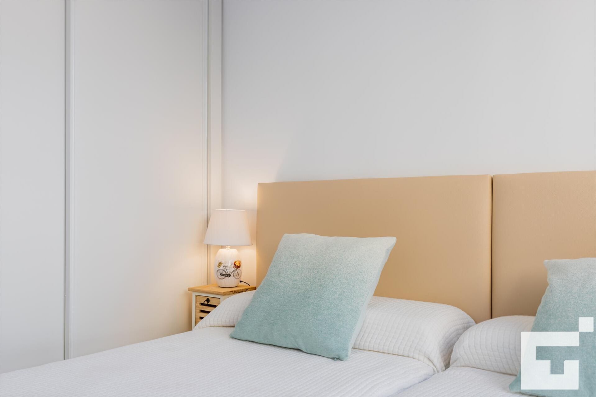A neatly made bed with a headboard, a bedside lamp, and a small bedside table with a lamp and a decorative item.