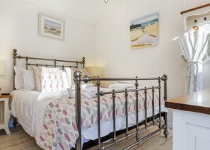 Una cama con ropa de cama estampada y bien hecha, una cama con dosel de estructura metálica, una mesita de noche con lámpara y un cuadro en la pared.