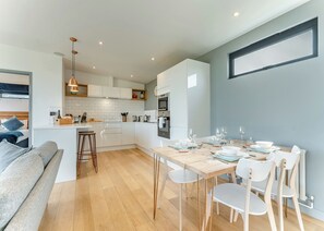 A modern kitchen with white cabinets, a wooden dining table, and bar stools.