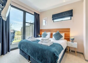 A modern bedroom with a large bed, a bedside table, a nightstand, a window with curtains, and a view of the outdoors.