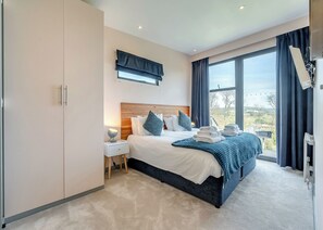 A modern bedroom with a large bed, a nightstand, a wardrobe, and a view of the outdoors.