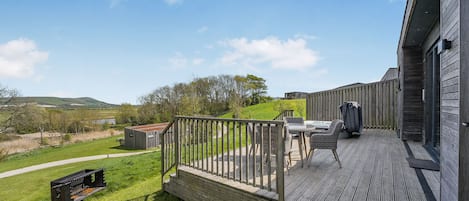 A wooden deck with outdoor furniture, a hot tub, and a view of a green landscape.