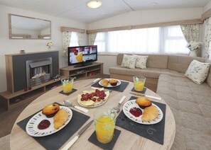 A furnished living room with a fireplace, television, sofa, and breakfast setup.