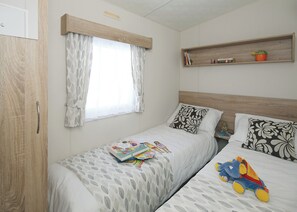 A bedroom with two beds, a window with curtains, a shelf with books and a plant, and a toy on one bed.