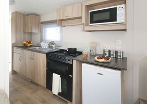 A compact kitchen with wooden cabinets, a microwave, a stove, and a small refrigerator.