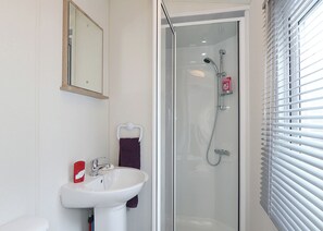 Ein Badezimmer mit einer Duschkabine, einem weißen Waschbecken und einem Spiegel.