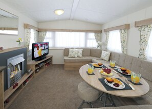 Ein gemütlicher Wohnbereich mit einer Couch, einem Fernseher, einem Kamin und einem Esstisch, der für das Frühstück gedeckt ist.