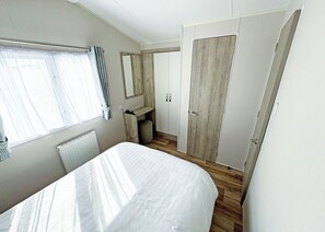 A bedroom with a bed, a wardrobe, a mirror, and a radiator. - Modern and contemporary 12ft-wide caravan with one double and two twin. (Bleadon, Weston-Super-Mare)