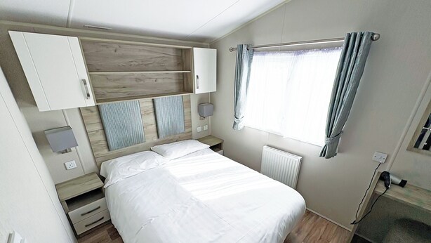 Een slaapkamer met een bed, een nachtkastje, een wandmeubel, een radiator en een raam met gordijnen.