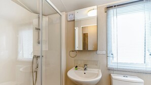 Een badkamer met een douchecabine van glas, een wastafel, een toilet en een raam met zonwering.