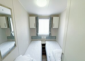 Un petit camping-car composé d’une seule pièce, avec deux lits, une fenêtre avec des rideaux et un miroir sur un des murs.
