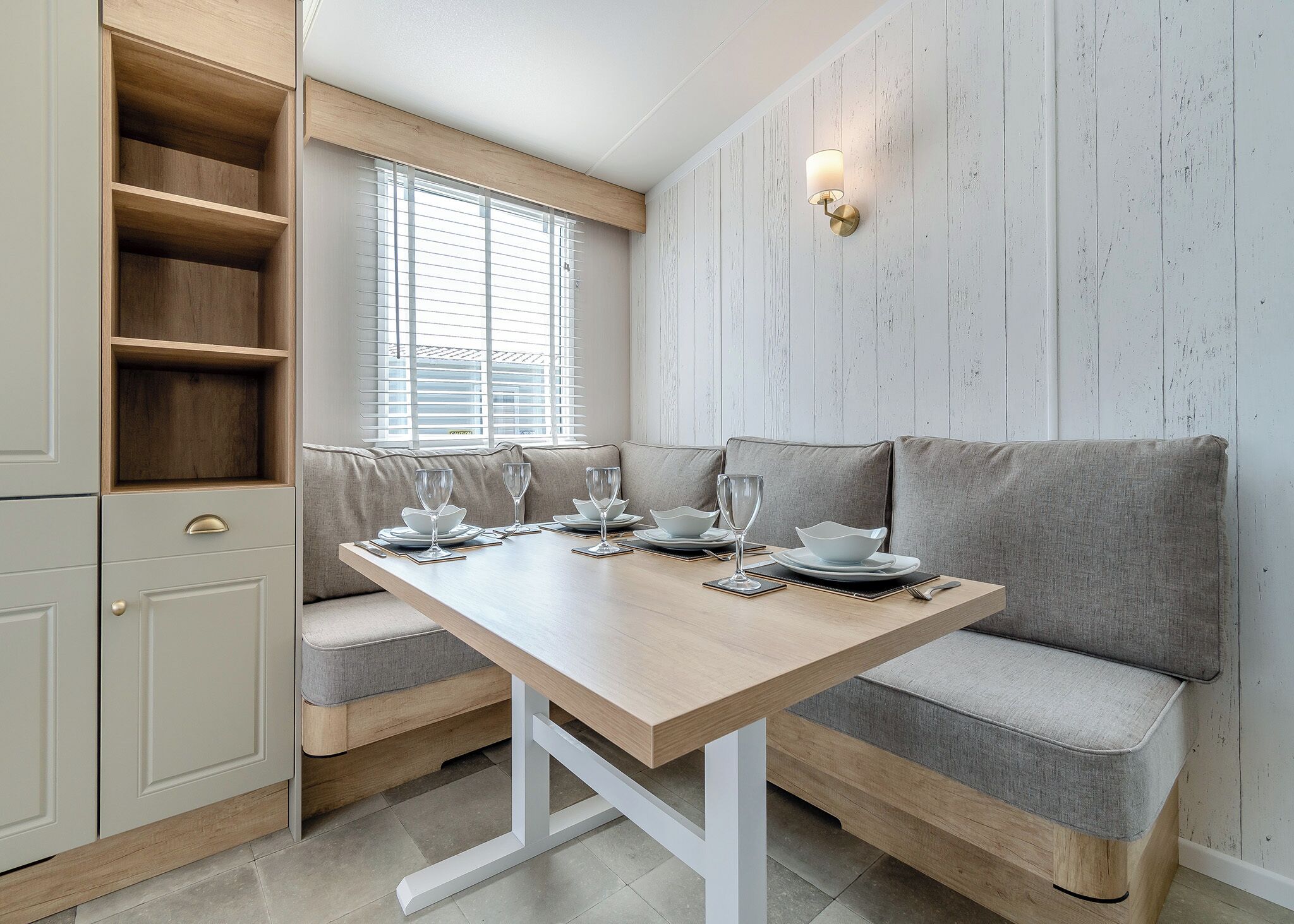 A dining area with a wooden table set for four, a grey sofa, and a built-in cabinet with shelves.