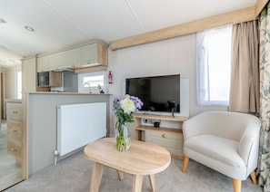 Un espacio habitable compacto con kitchenette, televisor de pantalla plana, sofá cómodo y una mesita con un florero.
