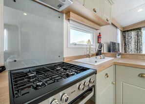 A modern kitchen with a gas stove, a sink, and a window. - Platinum Caravan 6 (Pet) (Skegness)
