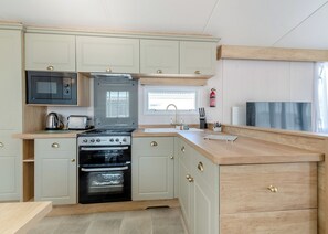 Cocina compacta con estufa, horno, microondas y ventana con persianas.