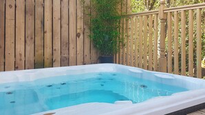 A hot tub in a wooden deck area with a wooden fence and a potted plant.