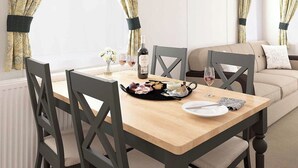 A dining area with a wooden table, four chairs, a bottle of wine, and a plate of food.