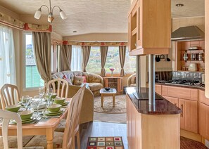A cozy room with a dining table set for four, a sofa, a kitchen area with a stove, and large windows with curtains.
