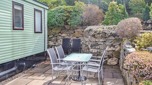 Une terrasse avec une table et des chaises, un mur en pierre et un bâtiment vert.