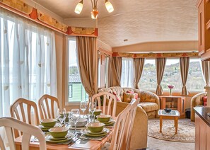A dining area with a table set for four, chairs, and a sofa. - Traditional yet comfortable caravan with one double and two twins. (Dolgellau)