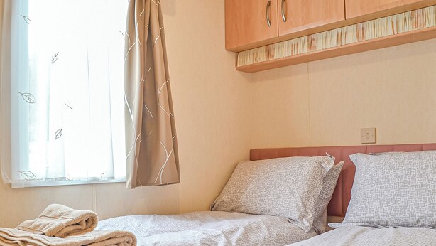 Une chambre d’hôtel avec deux lits, une fenêtre avec des rideaux et un meuble en bois placé au-dessus des lits.