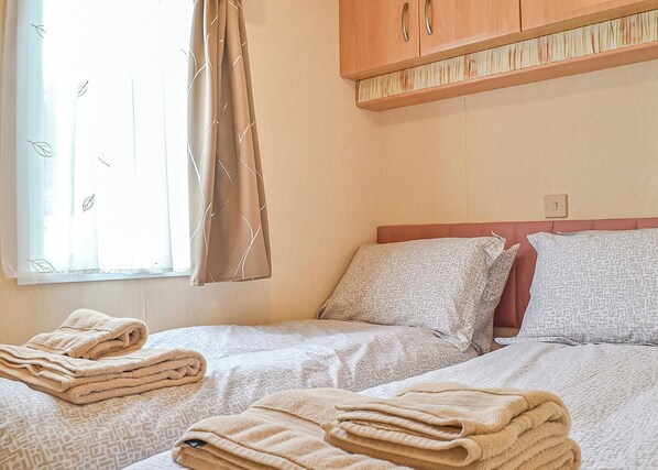 Hotellihuone, jossa on kaksi sänkyä, ikkuna, jossa on verhot, ja sänkyjen yläpuolella oleva puinen kaappi.