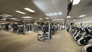 Een sportschool met diverse fitnessapparaten, waaronder loopbanden en krachtapparaten, gerangschikt in rijen.