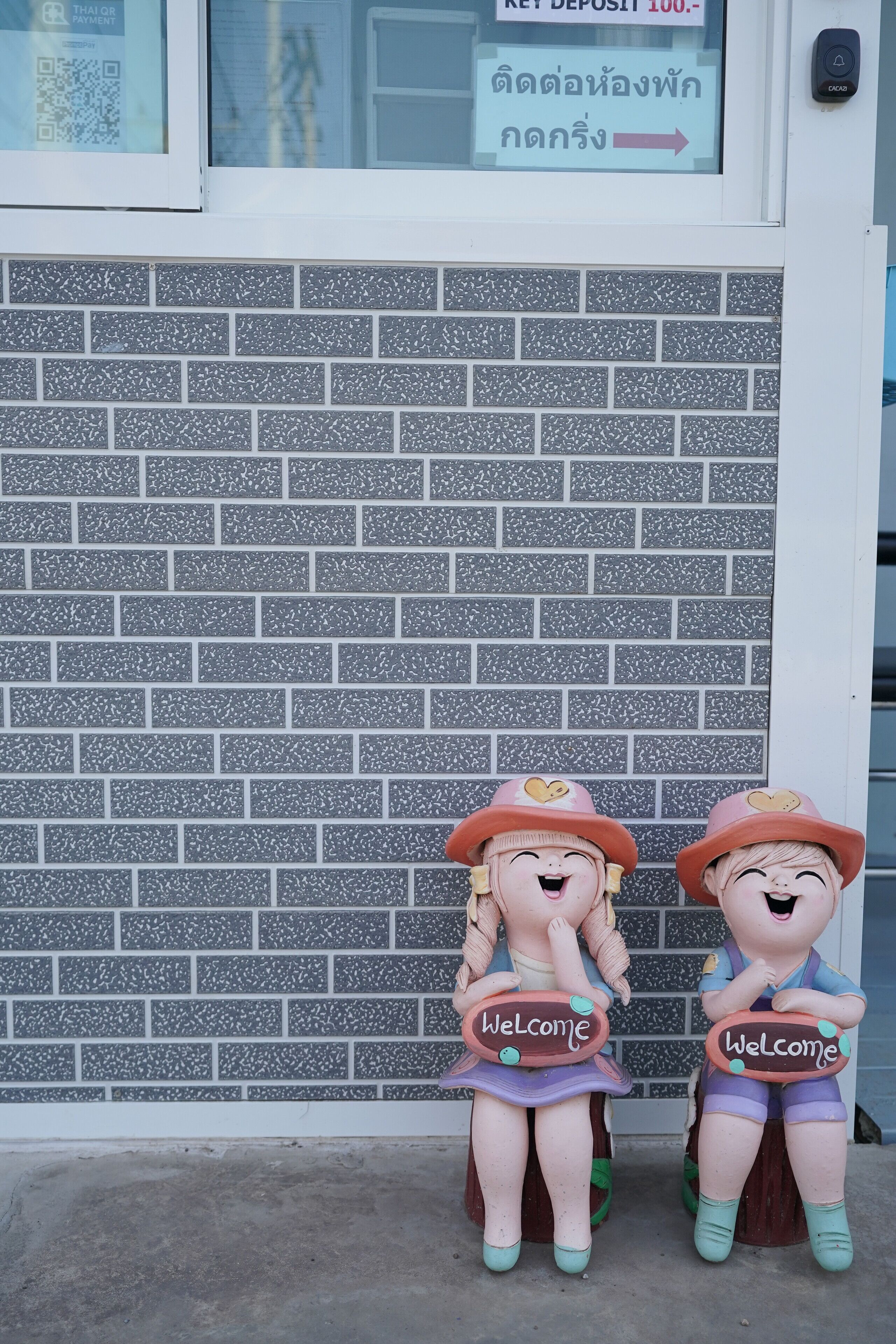 Duas figuras decorativas seguram placas com a palavra 'Welcome'.