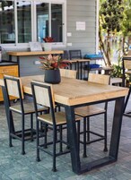Un área de comedor al aire libre con una mesa y sillas de madera, una planta en maceta y una ventana al fondo.
