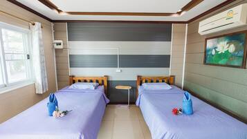 A hotel room with two beds, a small table, an air conditioning unit, and a painting on the wall.