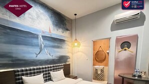 A hotel room with a large bed, a painting of dolphins, a hanging light fixture, a wardrobe, and a small table with toiletries. - Hotel Pantes Candi Semarang (Semarang)