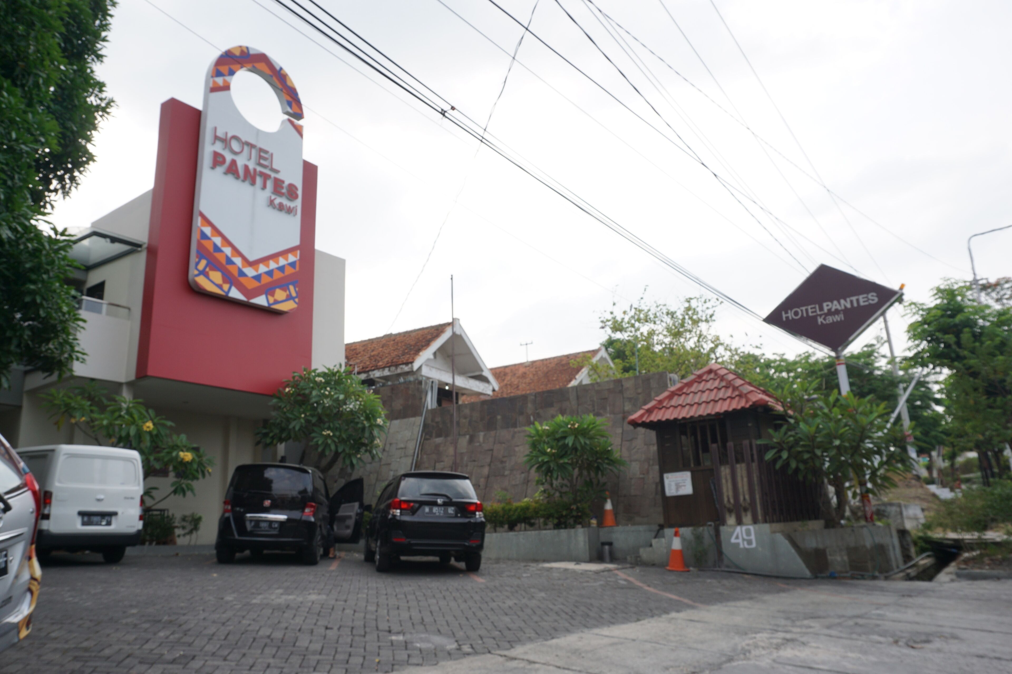 A hotel entrance with a prominent sign, a paved driveway, and parked cars.