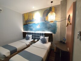 Habitación de hotel con dos camas, un cuadro de un paisaje, una mesita de noche con una lámpara y un escritorio pequeño con un teléfono y botellas de agua.