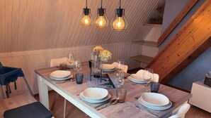 A dining area with a wooden table set for four, including plates, glasses, and cutlery. There are three hanging light fixtures above the table. - Waldrauschen by Interhome (Bad Arolsen)