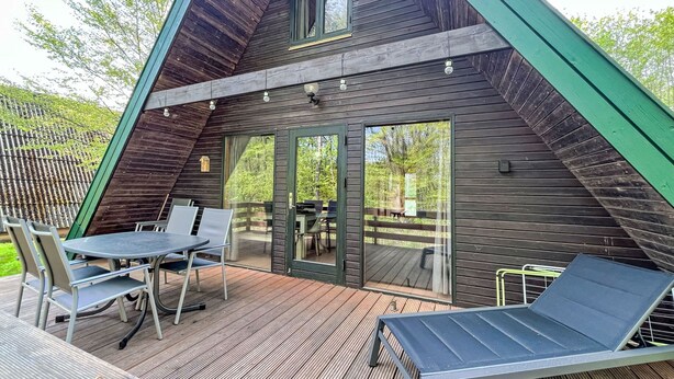 A wooden A-frame cabin with a deck, a table with chairs, and a lounge chair. - Waldrauschen by Interhome (Bad Arolsen)