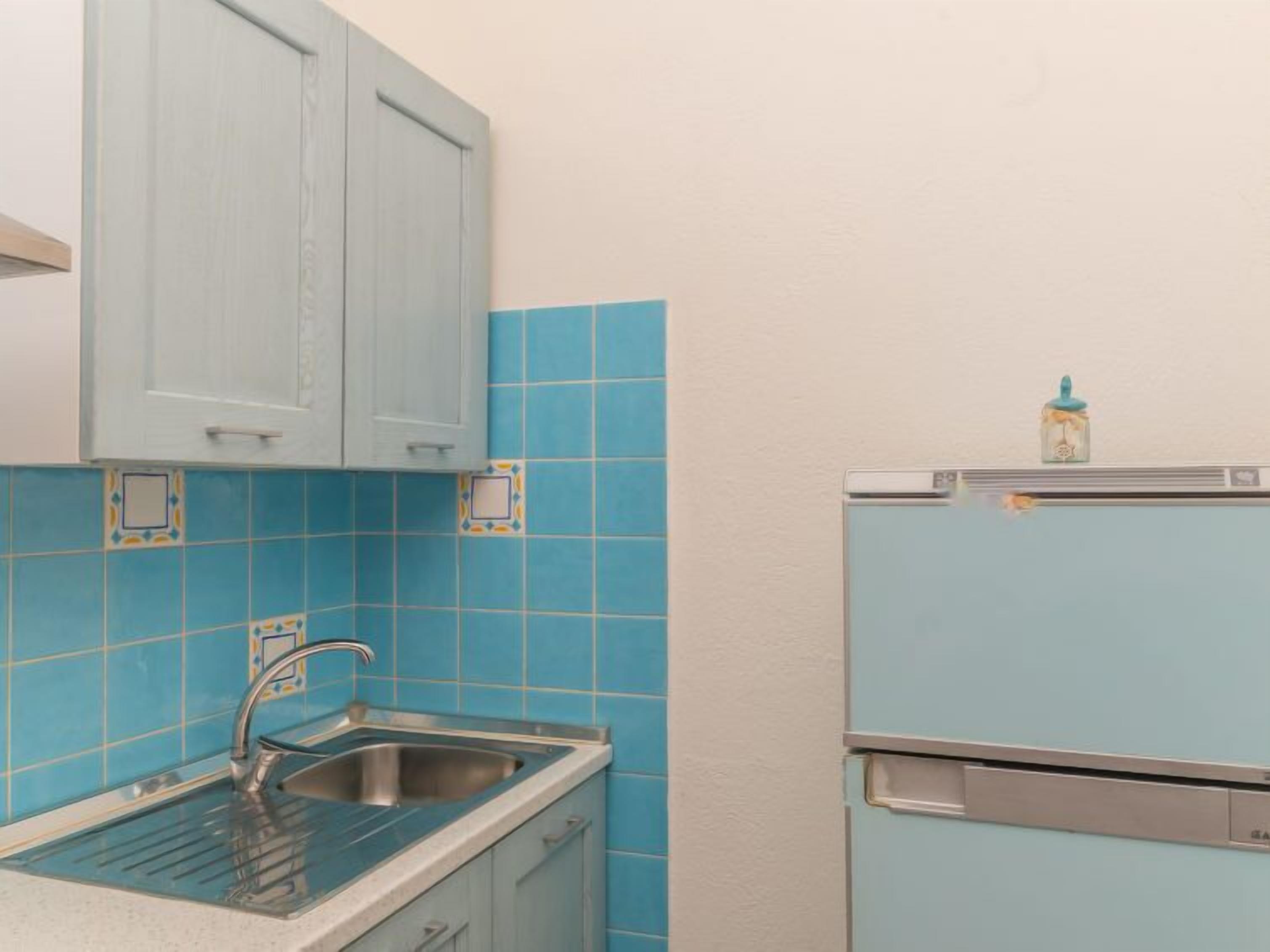 Eine Küche mit blauen Fliesen, einer Edelstahl-Spüle und einem hellblauen Kühlschrank.