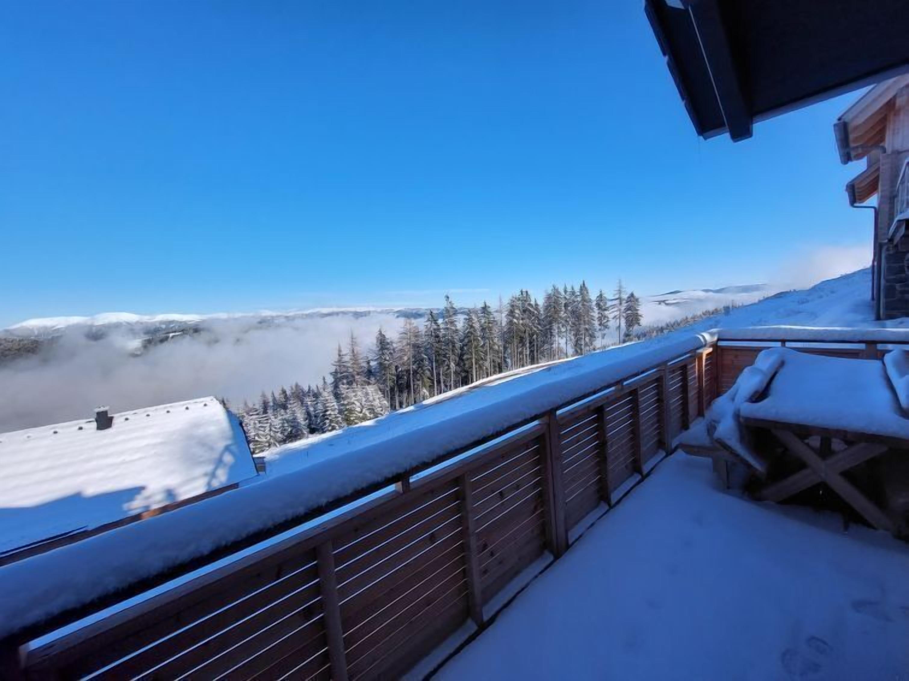 Un balcón cubierto de nieve con vistas a un bosque y montañas.