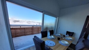 Un coin repas avec une table en bois dressée pour quatre personnes, de grandes fenêtres et une vue sur un paysage enneigé.
