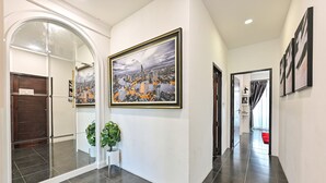 A hallway with a glass door leading to a room, a large framed cityscape painting on the wall, and a tiled floor. - Exquisite Pool Villa A  (Pattaya)