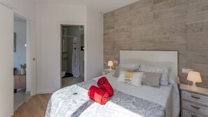 Quarto com uma cama, duas mesas de cabeceira, cabeceira de madeira e um banheiro visível por uma porta aberta.
