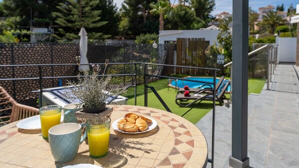 A patio with a table, chairs, a potted plant, and a pool in the background.