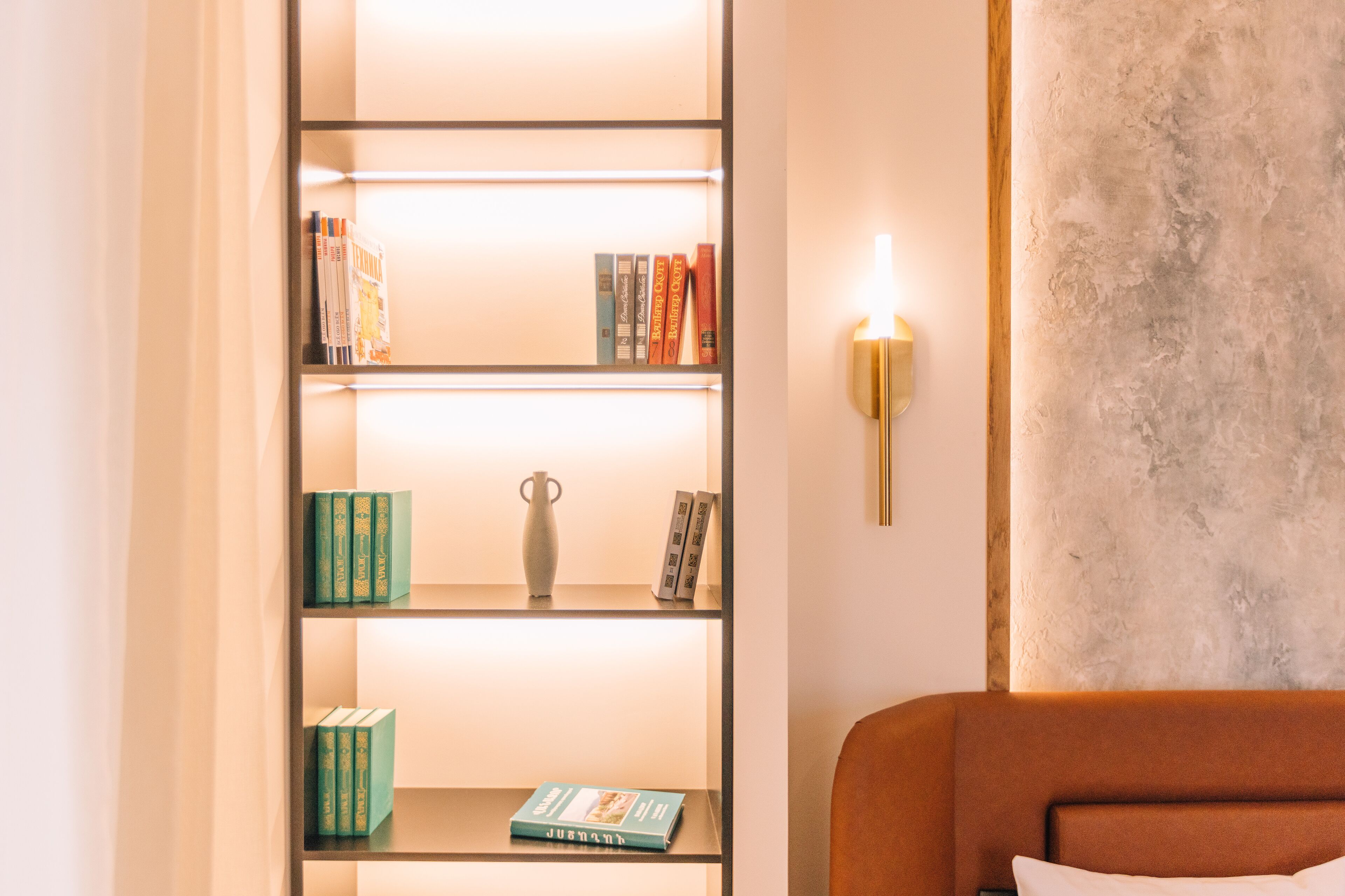 A bookshelf with books and a vase, a wall-mounted light, and a textured wall.
