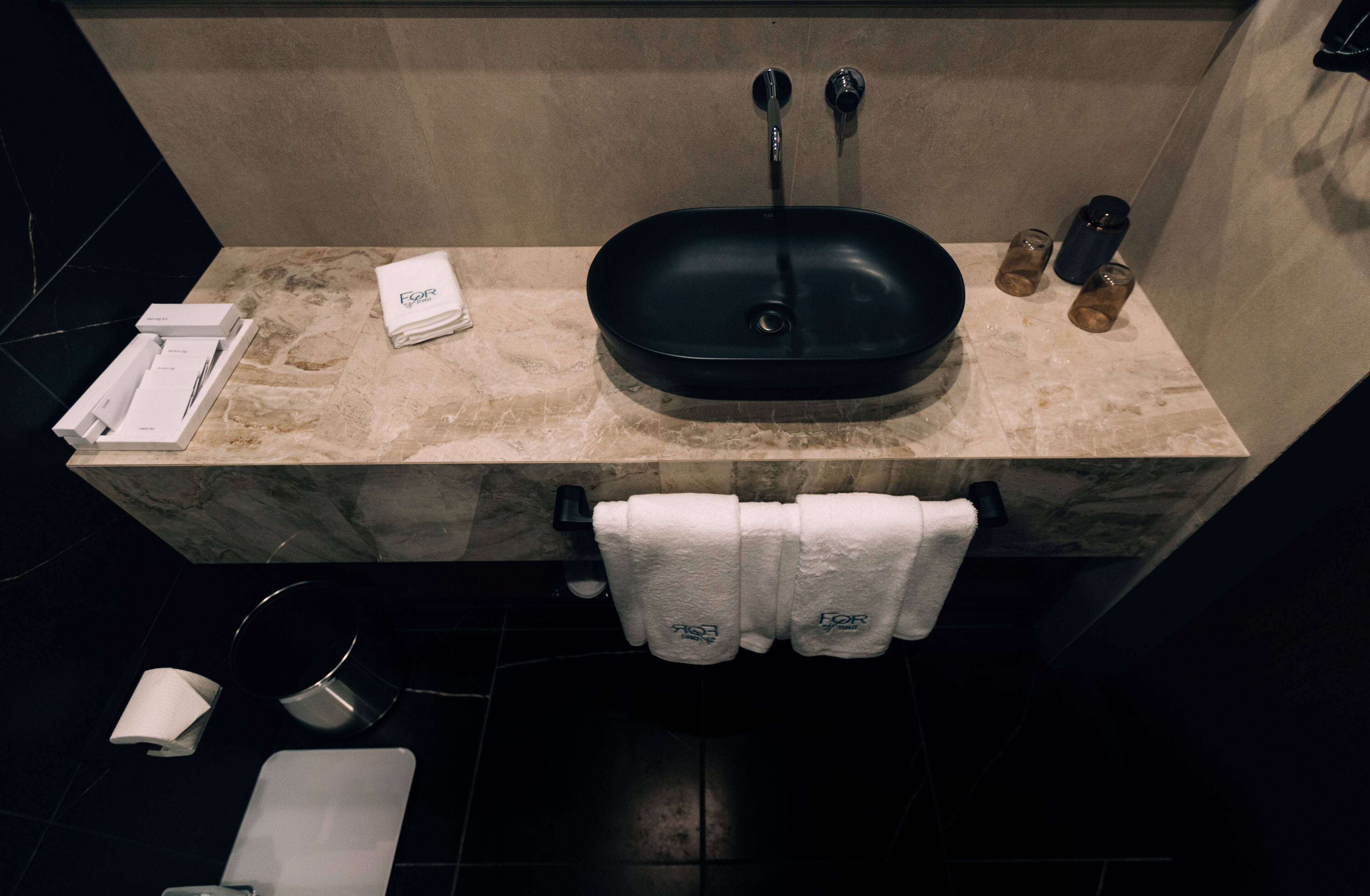 A bathroom with a black sink, marble countertop, and a towel rack with folded towels.