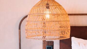 Un lit avec une literie blanche, une lampe en osier et une petite table ronde avec un pied noir.