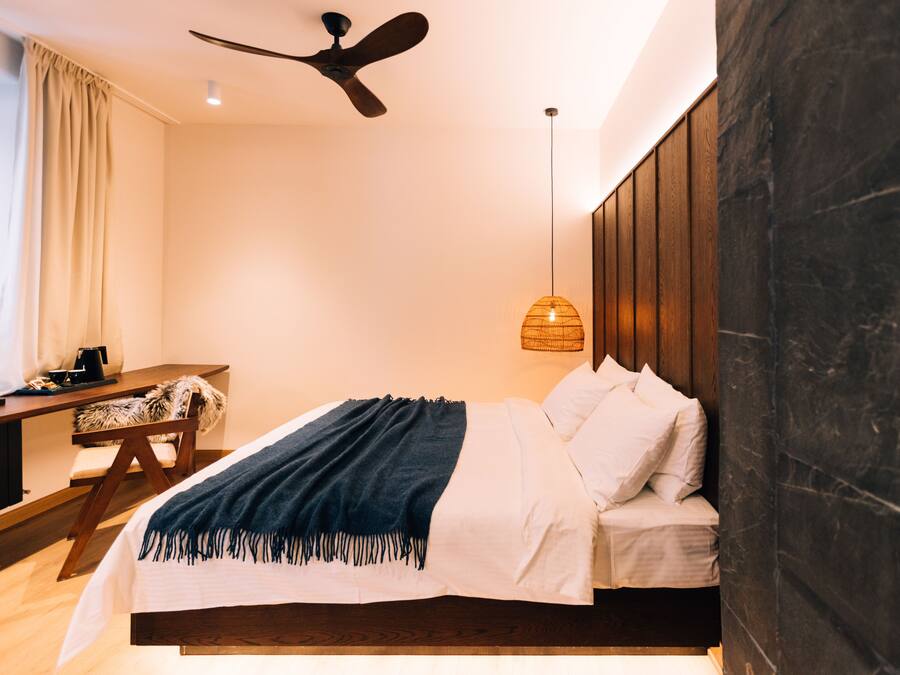 A modern bedroom with a bed, a desk, and a ceiling fan.