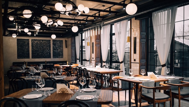 A restaurant with multiple tables set for dining, large windows with curtains, and hanging spherical light fixtures. - FORest 1961 Hotel & Restaurant (Vanadzor)