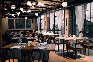 Un restaurante con varias mesas dispuestas para comer, amplias ventanas con cortinas e lámparas esféricas colgantes.