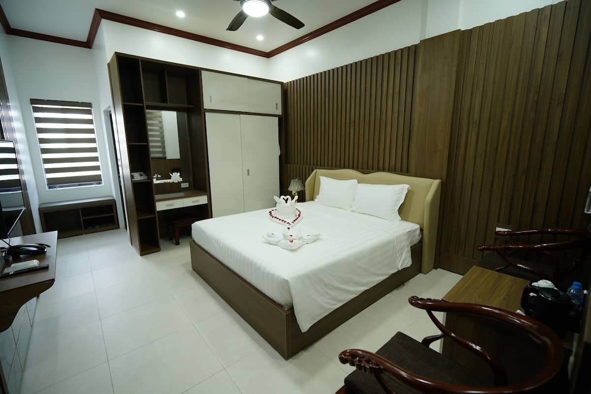 Une chambre d’hôtel équipée d’un lit, d’un bureau, d’une chaise, d’une armoire et d’un ventilateur de plafond.